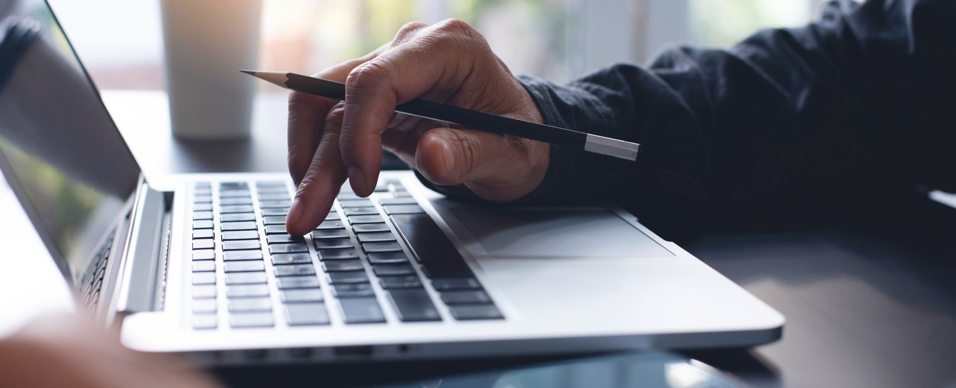 close up of adult hands typing on a laptop keyboard also holding a pencil